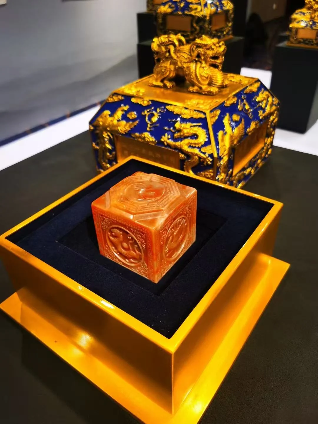A carved seal displayed in a presentation box beside a patterned cover